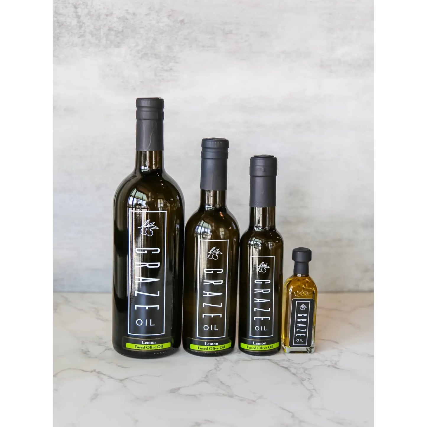 Four bottles of Graze Oil on a marble surface with a light gray background