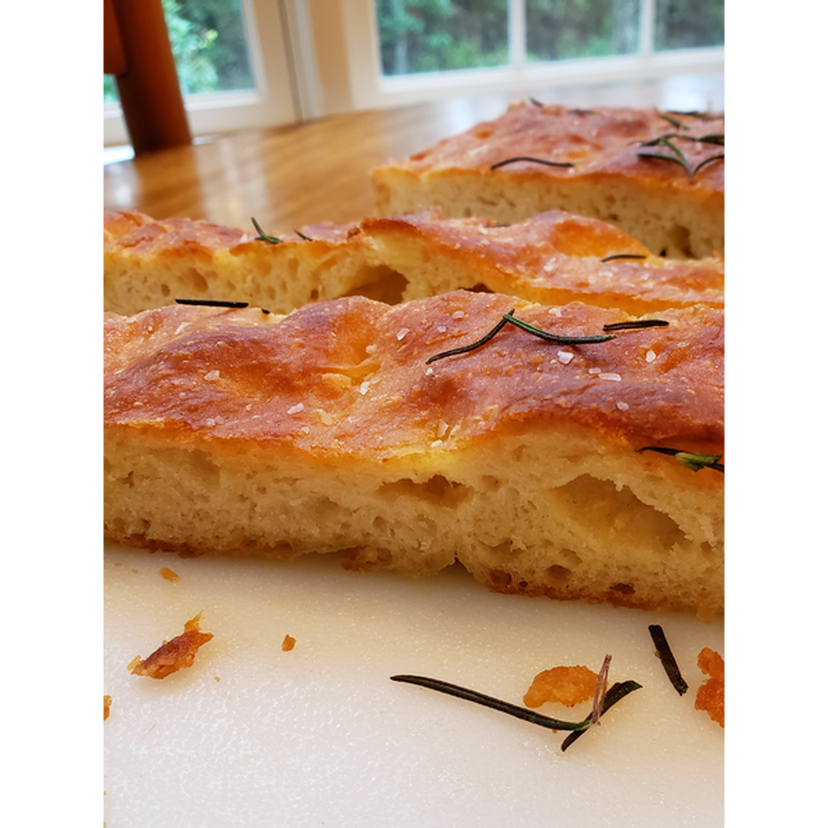 Close-up of a focaccia bread with rosemary on a white surface
