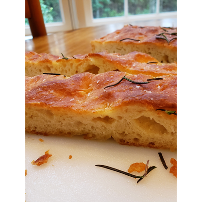 Close-up of a focaccia bread with rosemary on a white surface