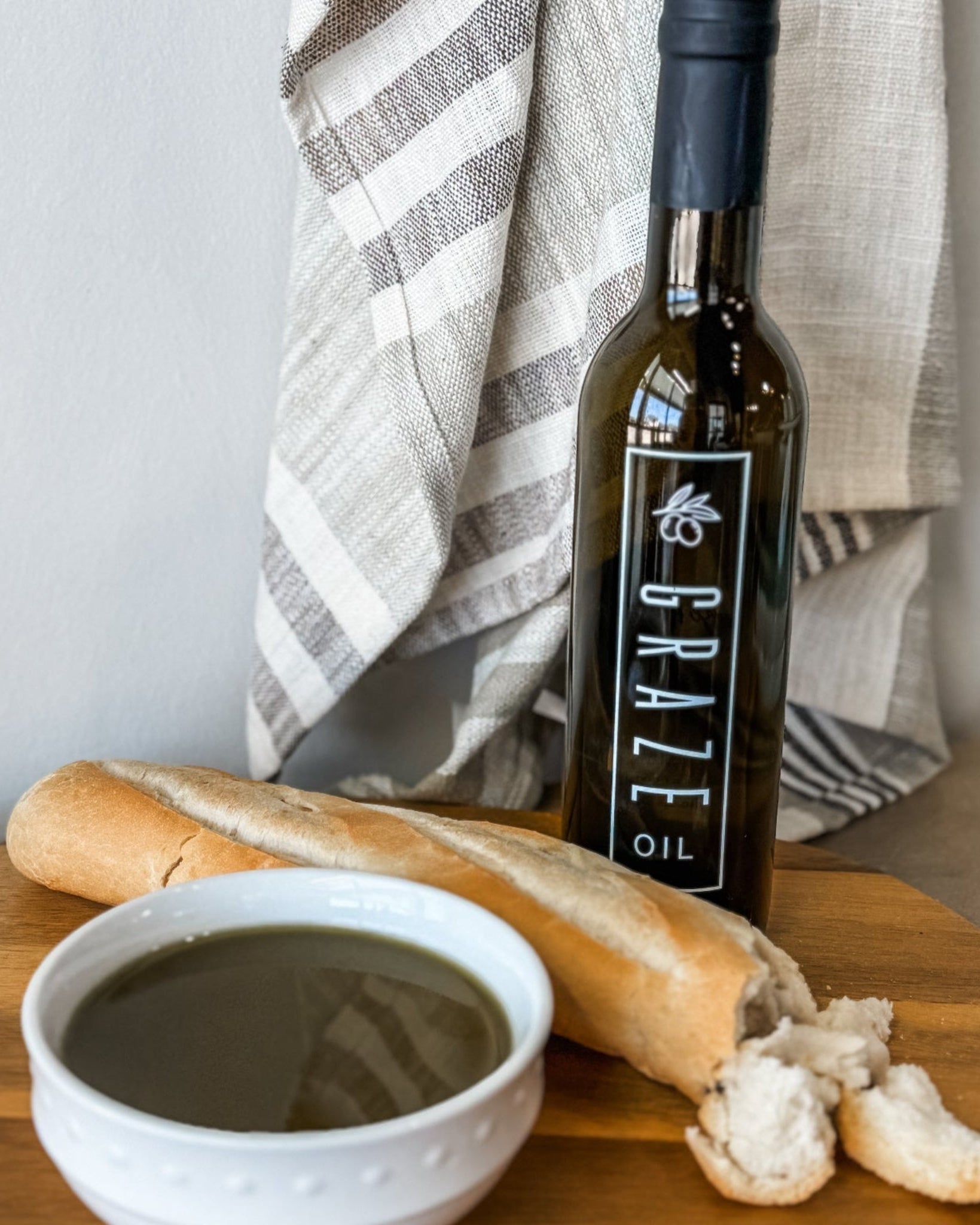 Bottle of Graze olive oil with a baguette and bowl on a wooden surface