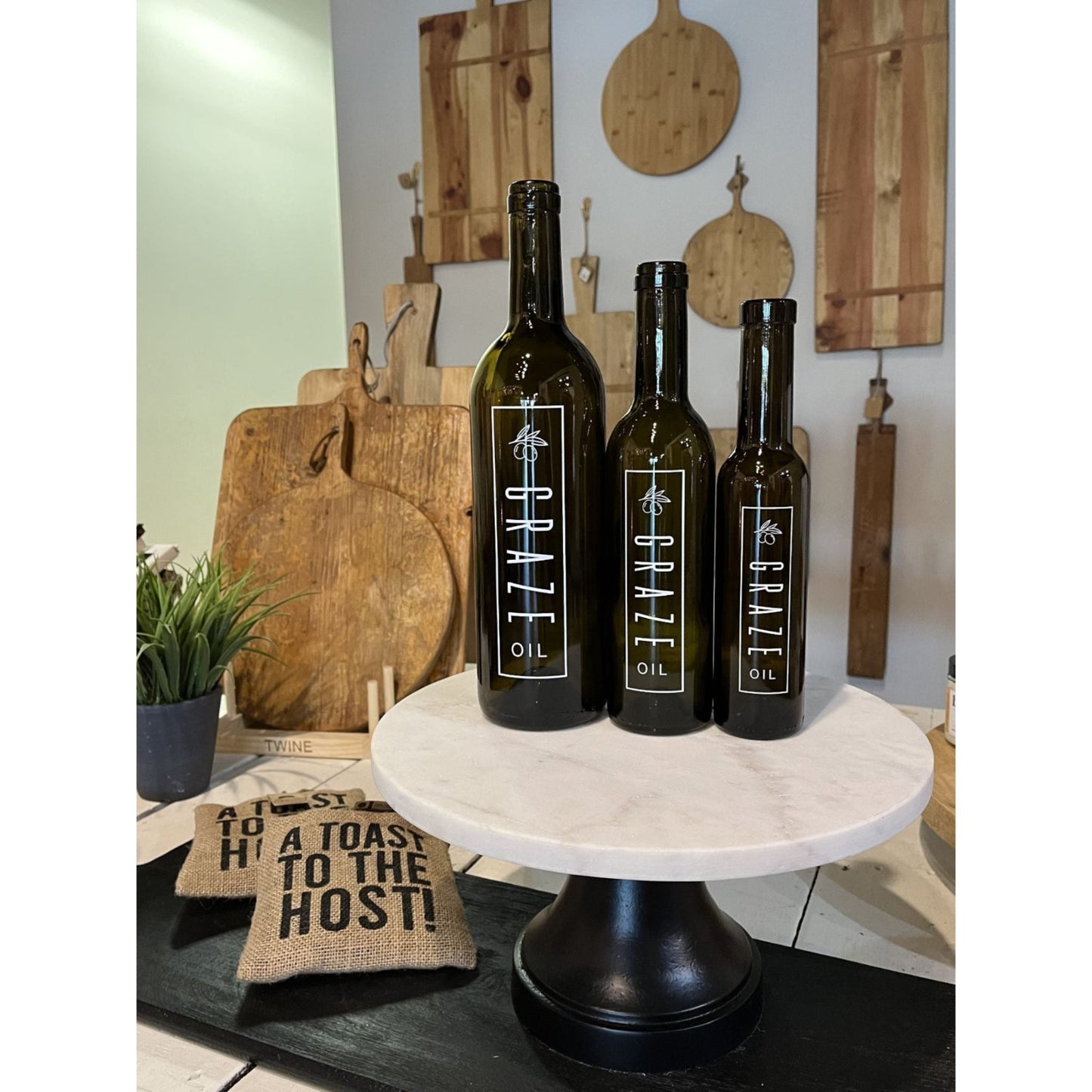Three bottles of Graze Oil on a marble stand with wooden cutting boards in the background.