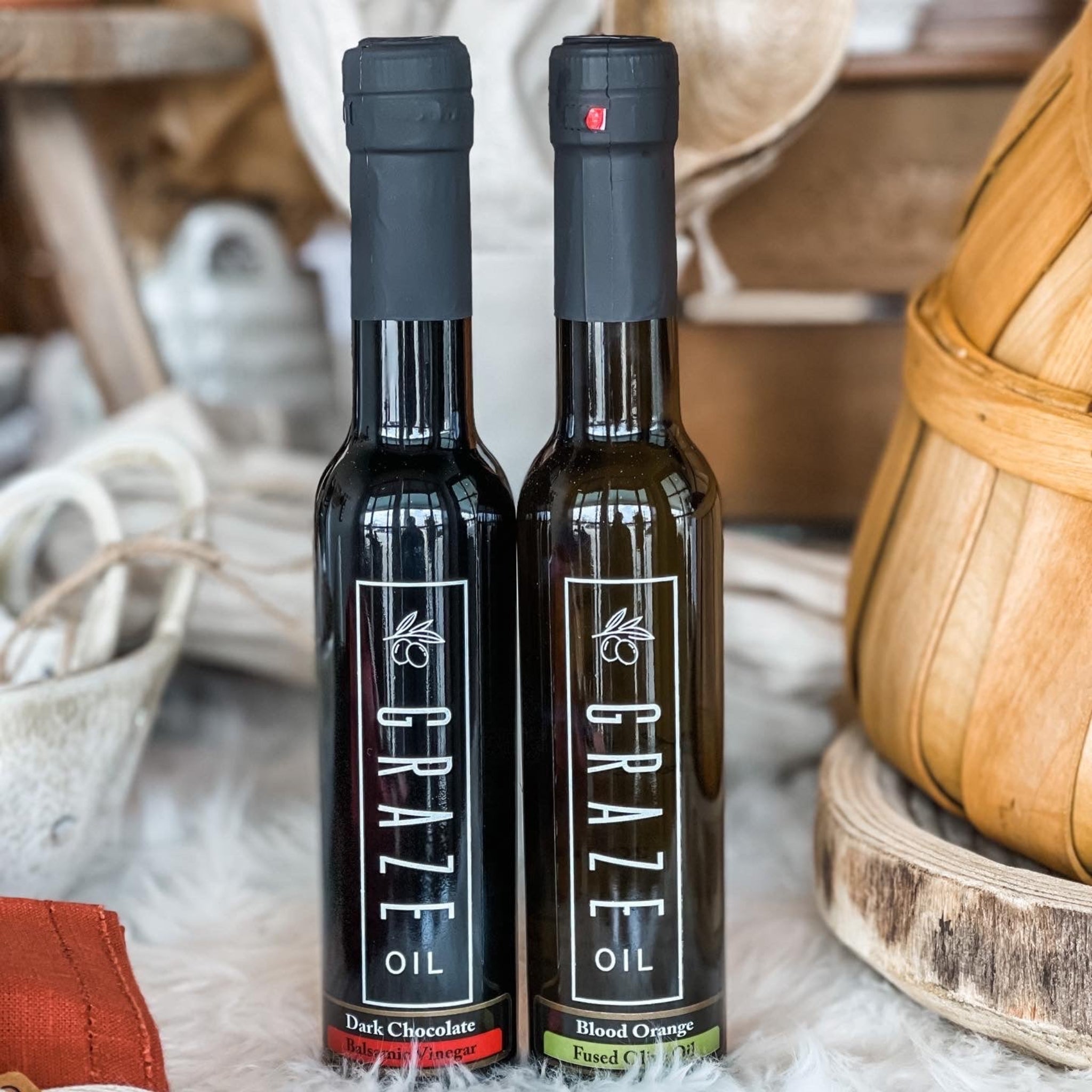 Two bottles of Graze Oil on a rustic surface with wooden and fabric elements.