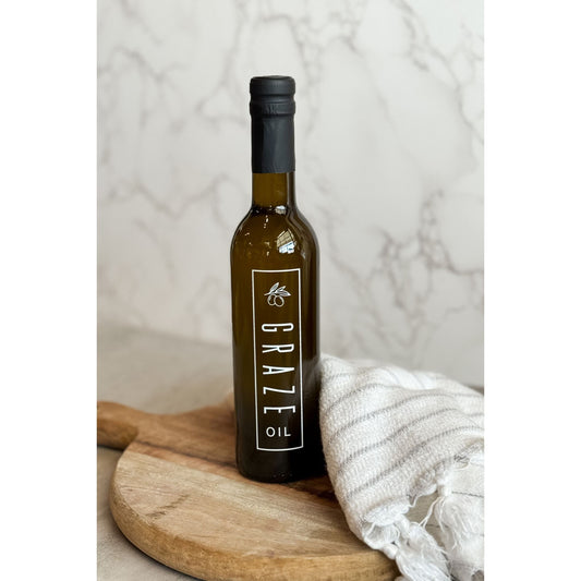 Bottle of Graze Oil on a wooden board with a white textured background