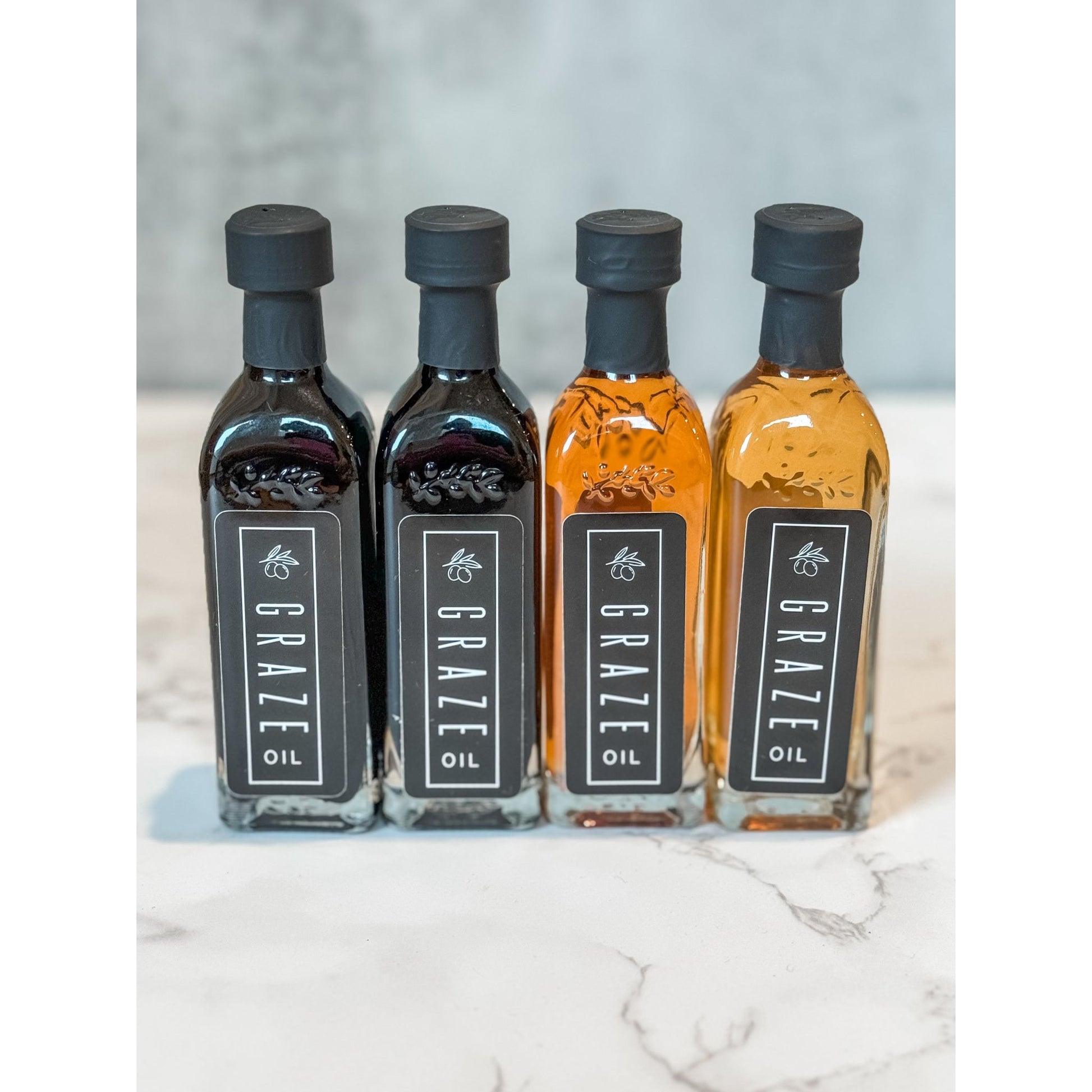 Four bottles of Graze Oil mini bottles on a marble surface with a light gray background