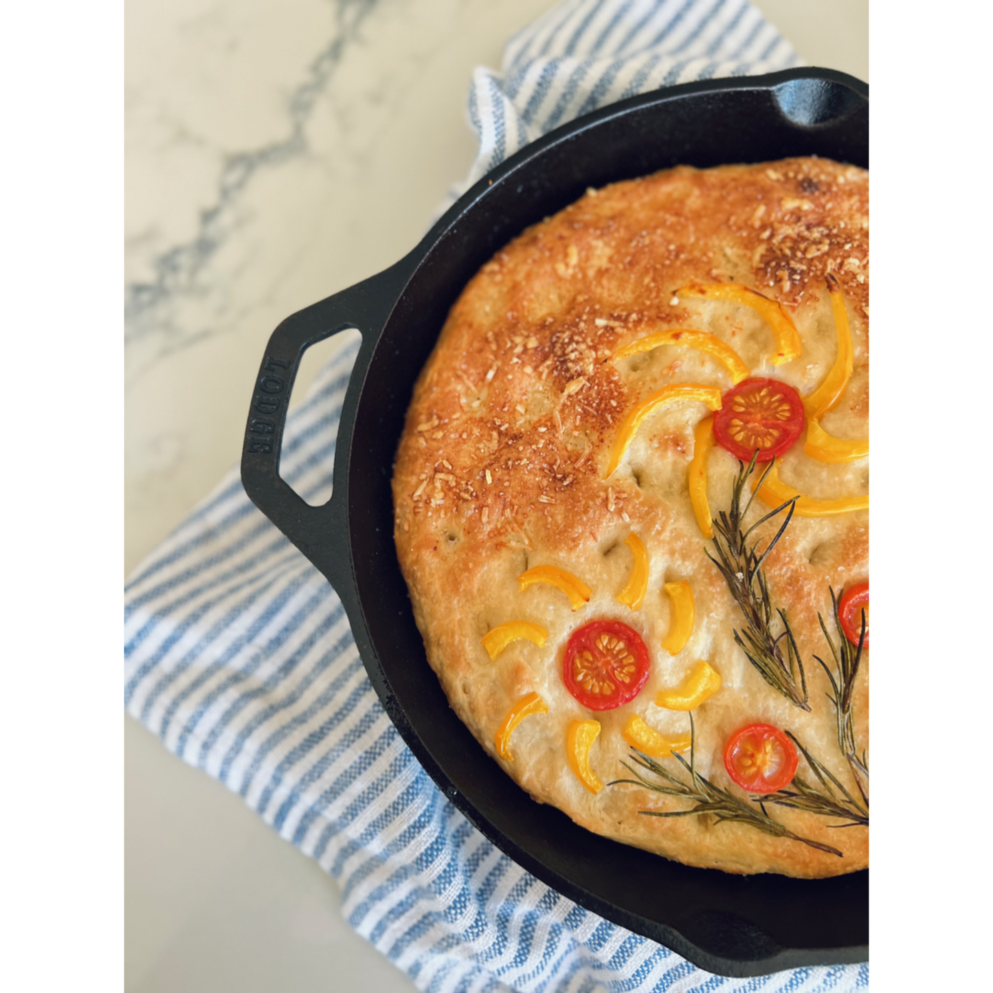 Focaccia bread with vegetables in a black skillet on a marble surface