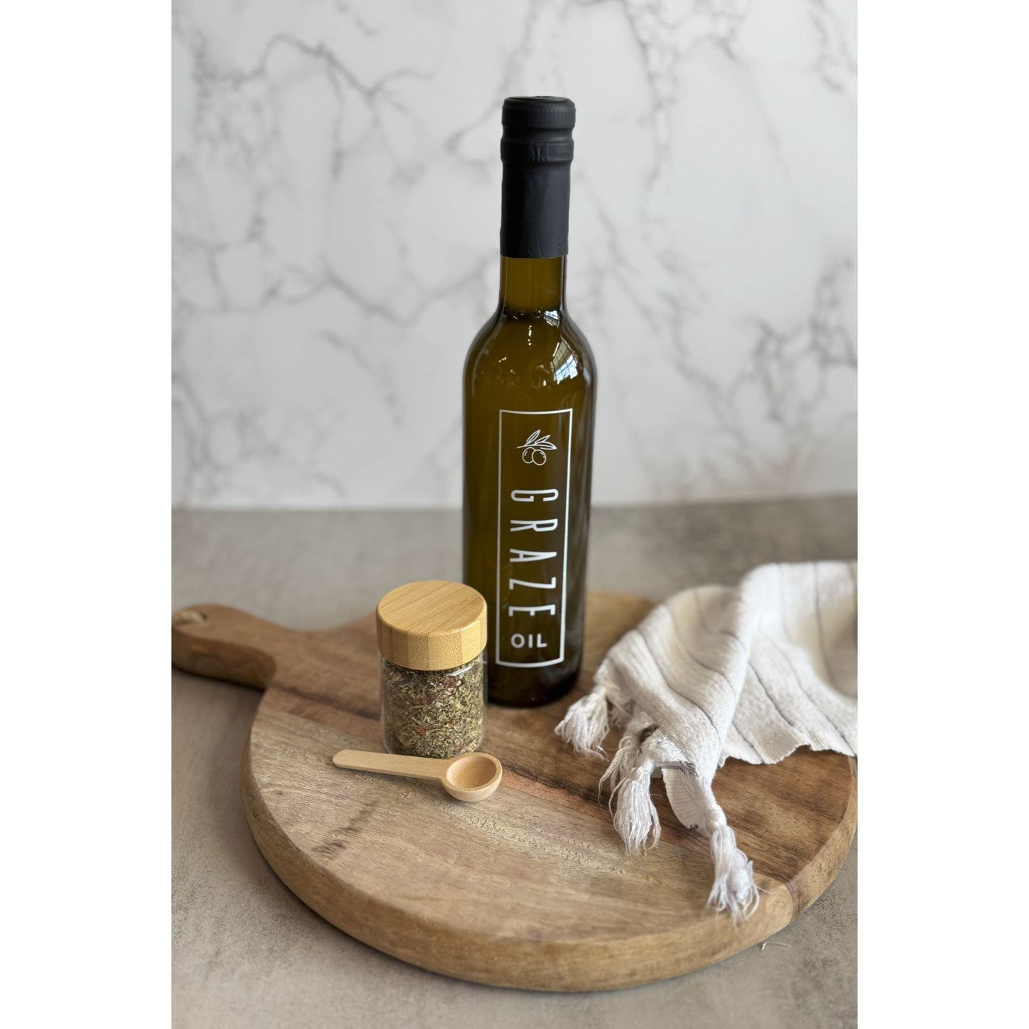 Bottle of olive oil with a wooden spoon and jar on a marble surface