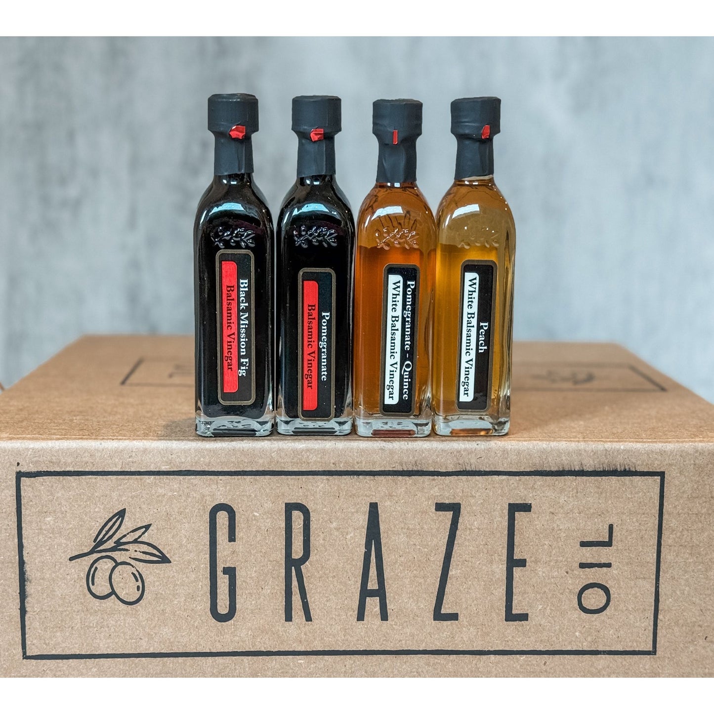 Four mini Graze Oil bottles of different types of olive oil and vinegar on a box labeled 'Graze oil'.